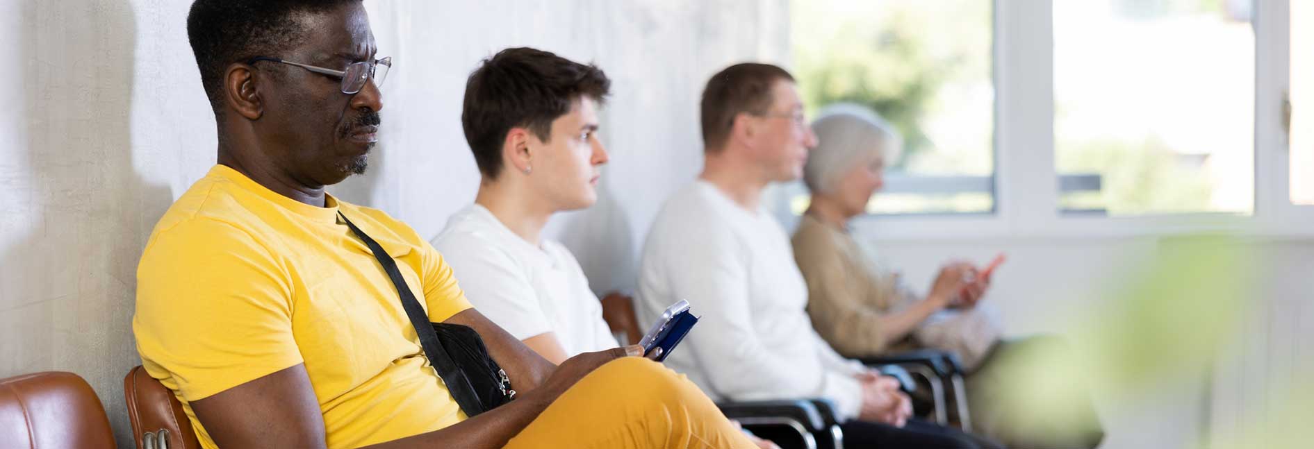 A man and other patients sitting with phone in lobby of medical clinic